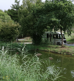 Ein Fischteich mit einem weißen Wohnmobil unter Bäumen. Elztal im Odenwald | © Erhard und Elvira Schneider "Zum Forellenbauer" GbR