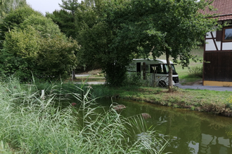 Ein Fischteich mit einem weißen Wohnmobil unter Bäumen. Elztal im Odenwald | © Erhard und Elvira Schneider "Zum Forellenbauer" GbR