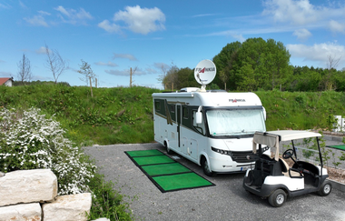 Ein weißes Wohnmobil, davor ein weißes Golfcart. Ein grüner Teppich liegt davor. Im Hintergrund eine grüne Wiese mit Bäumen. Mudau im Odenwald. | © Golfclub Mudau und Freizeitanlagen GmbH