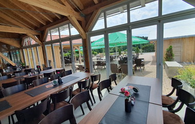 Ein Restaurant mit Tischen und Stühlen und großen Fenstern. Blick auf einen Biergarten mit grünen Schirmen. Mudau im Odenwald. | © Golfclub Mudau und Freizeitanlagen GmbH