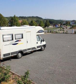 Ein weißes Wohnmobil im Vordergrund auf einem Stellplatz. Im Hintergrund ein kleines Wohnmobil. Hardheim im Odenwald.
