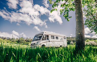 Weißes Wohnmobil fährt auf einer Straße. Im Vordergrund ist eine Blumenwiese im Hintergrund eine Streuobstwiese mit angrenzendem Wald. | Odenwald | © Touristikgemeinschaft Odenwald e.V.