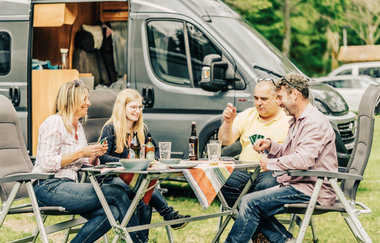 Zwei Frauen und zwei Männer sitzen an einem Campingtisch und spielen Karten. Im Hintergrund ist ein graues Wohnmobil. Odenwald. | © Touristikgemeinschaft Odenwald e.V.