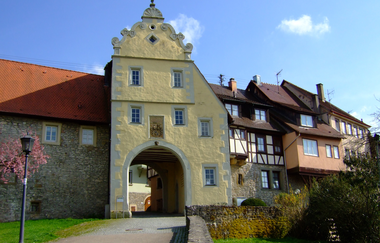 Das Tor ist gelb und hat einen Giebel. Daneben befinden sich Fachwerkhäuser auf der Stadtmauer | © Touristikgemeinschaft Hohenlohe e. V. | Stadt Forchtenberg