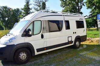 Blick auf den Wohnmobilstellplatz in Markelsheim.  Hier steht ein weißes Wohnmobil auf einer mit Rasengittersteinen ausgelegten Fläche. Im Hintergrund sind Bäume zu sehen. | © Unbekannt