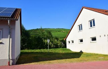 Blick auf einen Wohnmobilstellplatz in Markelsheim, eine Grünfläche zwischen zwei Gebäuden. Im Hintergrund sind die Weinberge zu sehen. | © Unbekannt