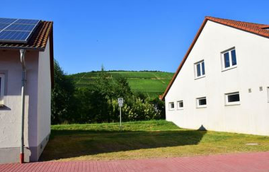 Blick auf einen Wohnmobilstellplatz in Markelsheim, eine Grünfläche zwischen zwei Gebäuden. Im Hintergrund sind die Weinberge zu sehen. | © Unbekannt