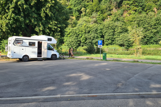 Geteerter Wohnmobilstellplatz mit einem weißen Wohnmobil daneben stehen zwei Frauen. Hinter dem Wohnmobil fliesst der Neckar. | Neckargerach | Odenwald | © Gemeinde Neckargerach