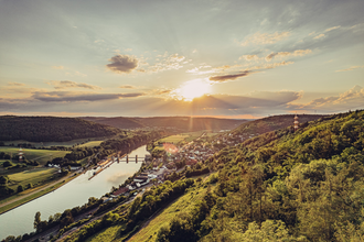 Weitblick mit Sonnenuntergang auf einen Fluss. Auf der rechten Uferseite erstreckt sich eine Gemeinde. Neckarzimmern im Odenwald. | © Touristikgemeinachaft Odenwald e.V.