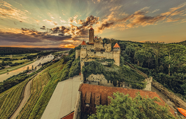 Blick auf eine Burg die auf einem Berg steht. Auf der linken Seite fließt ein Fluss auf der rechten Seite ist ein Wald. Burg Hornberg im Odenwald. | © Touristikgemeinachaft Odenwald e.V.