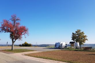 Blick auf einen Parkplatz mit einem Wohnmobil. Daneben steht eine Infotafel, ein Baum und eine Sitzgelegenheit. Neunkirchen im Odenwald.