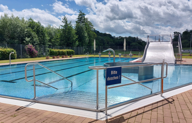 Es ist ein Freibad mit einer Treppe zu sehen. Auf der anderen Seite des Bads gibt es eine breite Stahlrutsche. Schefflenz im Odenwald | © Gemeinde Schefflenz