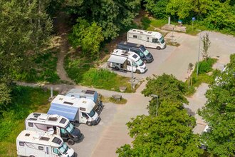Wohnmobilstellplatz mit mehreren geparkten Wohnmobilen, umgeben von Bäumen. | © Michael Kühneisen