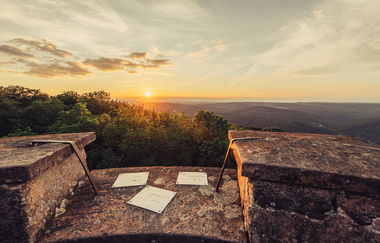 Man sieht den Rand eines Steinturmes mit 3 Plaketten und Blick in die Weite und den Sonnenuntergang. Odenwald. | © Touristikgemeinschaft Odenwald e.V.