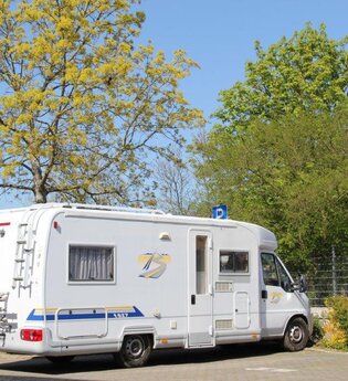 Blick auf den Wohnmobilstellplatz in Tauberbischofsheim. Hier ist ein Wohnmobil neben Bäumen auf einem asphaltierten Platz zu sehen. | © Stadt Tauberbischofsheim