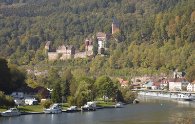Blick auf eine Flußbierung mit Booten am linken Ufer. Im Hintergrund ist ein großen Schloß auf einem bewaldeten Hügel zu sehen. Zwingenberg im Odenwald. | © Touristikgemeinschaft Odenwald e.V.
