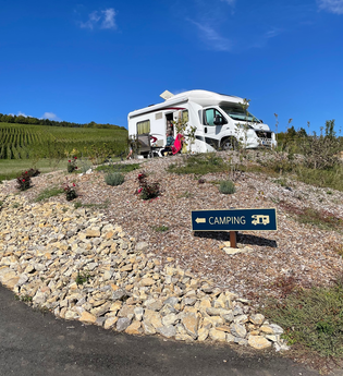 Blick auf den am Rand der Weinberge gelegenen Wohnmobilstellplatz Weingut Ehrmann.  Hier steht ein Wohnmobil. Bei schönstem Wetter und blauem Himmel genießen die im Freien sitzenden Gäste den Ausblick. | © Touristinfo Weikersheim