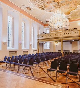 Ein Konzertsaal mit einem Flügel, leeren Stuhlreihen und einem Kronleuchter an der Decke. | © Kulturstiftung Hohenlohe