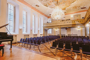 Ein Konzertsaal mit einem Flügel, leeren Stuhlreihen und einem Kronleuchter an der Decke. | © Kulturstiftung Hohenlohe