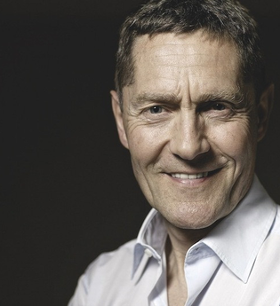 Porträt eines lächelnden Mannes in einem weißen Hemd vor dunklem Hintergrund. | © Kulturstiftung Hohenlohe