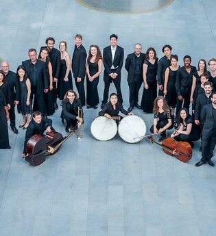 Eine Gruppe von Musikern in schwarzer Kleidung steht in einem Kreis auf einem grauen Boden. | © Kulturstiftung Hohenlohe