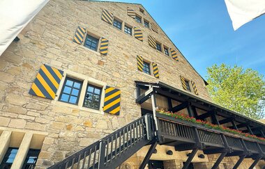 Außenansicht der Herzogskelter in Güglingen mit gelb-schwarz gestreiften Fensterläden und einer Holzbalustrade