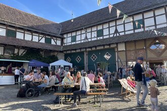 Hoffest ist zu sehen mit Menschen auf Bierbänken im Hintergrund sind die Gebäude des Bauernhofs zu sehen | © Biohof Groß