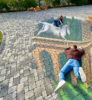 Zwei Personen interagieren mit einer 3D-Straßenmalerei, die eine Brücke und ein Einhorn darstellt. | © Erlebnispark Tripsdrill