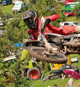 Ein Motorradfahrer in roter Kleidung mitten im Sprung, im Hintergrund Zuschauer | © Rainer Kengeter