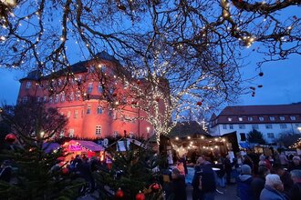 Blick auf den festlich geschmückten Weihnachtsmarkt in Künzelsau mit Schloss Bartenau im Hintergrund