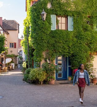 Zwei Frauen spazieren durch eine malerische Altstadt mit Fachwerkhäusern und begrünten Fassaden. | © Stadt Besigheim