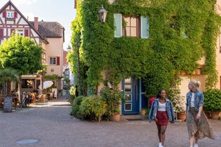 Zwei Frauen spazieren durch eine malerische Altstadt mit Fachwerkhäusern und begrünten Fassaden. | © Stadt Besigheim