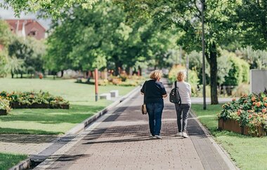 Zwei Frauen laufen auf der Grünspange, außenrum liegen Grünanlagen mit Blumenbeeten. | © Stadt Bad Rappenau I Chris Frumolt