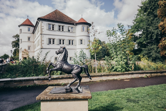 Wasserschloss im Hintergrund mit kleiner Statue des schwarzen Rappen auf Sockel im Vordergrund | © Stadt Bad Rappenau I Chris Frumolt