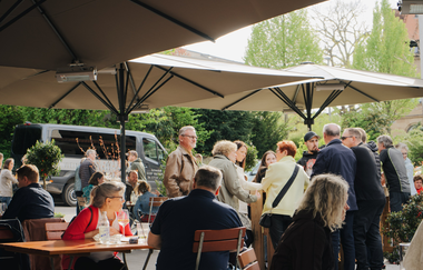 Außenbereich mit drei großen Sonnenschirmen und vielen Personen | © Christian Seyffer