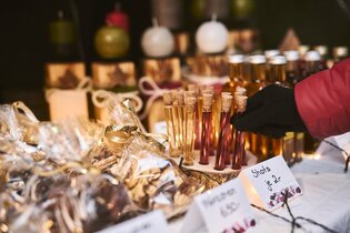 Produkte an einem Stand auf einem Weihnachtsmarkt (z.B. Shots und Gebäck). Eine Hand greift nach einem Shot im Reagenzglas. | © Touristikgemeinschaft Hohenlohe e.V. | Stefan Leitner Photography