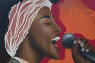 Graffiti einer Frau, die in ein Mikrofon singt, vor einem orange-roten Hintergrund. | © Petra Natzkowski