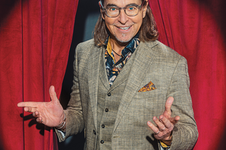 Künstler im Anzug steht vor einem roten Bühnenvorhang