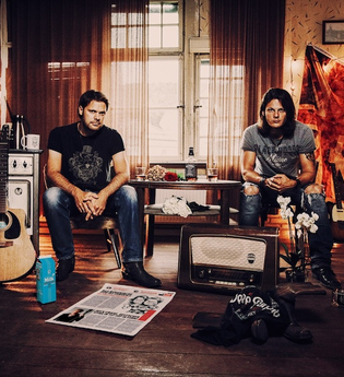 Zwei Männer sitzen in einem Raum mit Musikinstrumenten und Dekorationen. | © Kulturfenster Bönnigheim e. V.