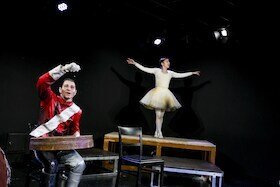 Foto der Zinnsoldat auf der Bühne, eine Tänzerin steht im Hintergrund auf einem Tisch in Ballerina-Pose | © Roland Schimmelpfennig