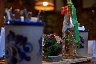 Tischdekoration mit Steingutkrügen, einer dekorierten Flasche und Blumenarrangement in einer Besenwirtschaft.