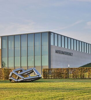 Das moderne Gebäude ist halb in die Erde gebaut, davor stehen zwei Skulpturen | © Touristikgemeinschaft Hohenlohe e. V. | Andi Schmid