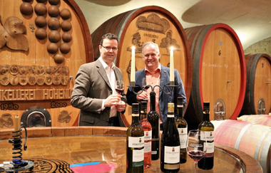 Zwei Männer halten ein Glas Wein in der Hand und stehen vor großen, schmucken Holzfässern | © Touristikgemeinschaft Hohenlohe e. V.