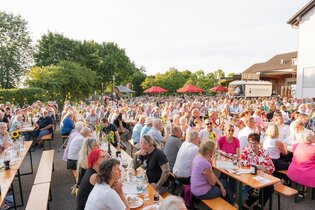 Viele Menschen sitzen auf Sitzbänken an Tischen beim FUERSTENFASS Sommerweinfest. | © Touristikgemeinschaft Hohenlohe e. V. | Samuel Eisel