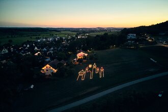 Luftaufnahme des Teilorts Goldbach, zu sehen ist eine Turmsilhouette aus Kerzen | © Julien Fertl