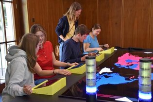 Einige Menschen sitzen am Spieletisch im Mark Twain Center. Es kann ein interaktives Strategiespiel gespielt werden.
