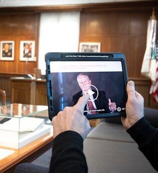 Im Vordergrund ein Tablet, das von einem Mann gehalten wird. Im Hintergrund ein großer Schreibtisch im Kommandantenzimmer des Mark Twain Centers.