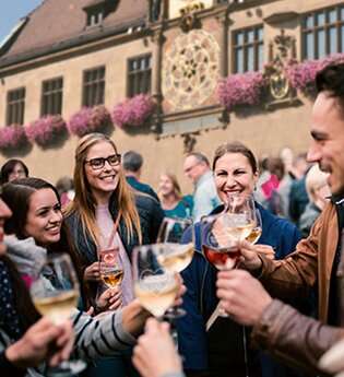 Fröhlich feiernde Gruppa an Gästen auf dem Marktplatz vor dem Rathaus. Alle haben ein Weinglas in der Hand und stoßen auf den schönen Abend auf dem Weindorf an. | © Heilbronn Marketing GmbH