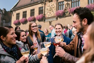 Fröhlich feiernde Gruppa an Gästen auf dem Marktplatz vor dem Rathaus. Alle haben ein Weinglas in der Hand und stoßen auf den schönen Abend auf dem Weindorf an. | © Heilbronn Marketing GmbH