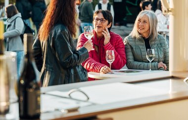 Frauen an einem Weinstand mit Weinbergen im Hintergrund